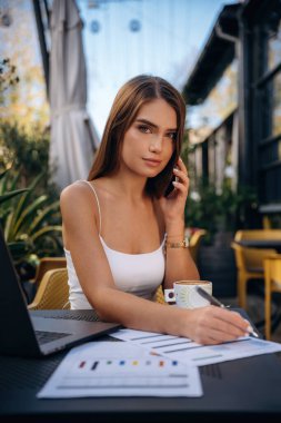 Telefon görüşmesi, belgelerle birlikte. Güzel, genç bir bayan restoranın dışında, masanın yanında..