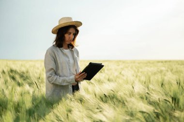 Hasır şapkalı, tabletli. Beyazlı kadın tarla tarlasında..