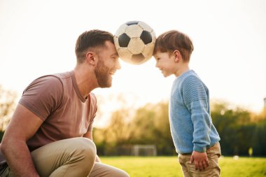Futbol topu, kafasından tutmak, eğlence. Mutlu baba ve oğlu yazın sahada olurlar..