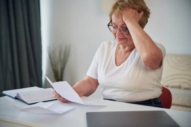 Gazetedeki bilgileri okuyorum. Yaşlı yaşlı kadın evde, oturma odasında..