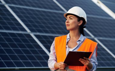 Not defteri elimde. Üniformalı kadın işçi mühendisi güneş panellerinin yakınında..