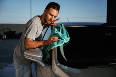 Turkuaz kumaş, aracı cilalama. Adam dışarıda arabasıyla bekliyor..