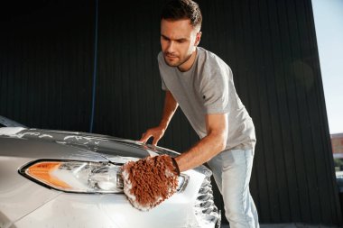 Otomobili yıkamaya odaklanmış. Adam dışarıda arabasıyla bekliyor..