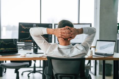 Ellerin başının arkasında oturuyorsun. İşadamı bilgisayar başında ve ofiste çalışıyor..