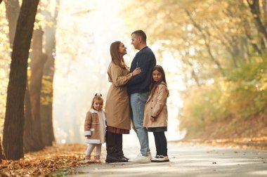 Sonbahar parkı. Anne, baba ve iki kızın mutlu aileleri ormanda, yolda.