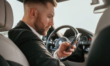 Siyah takım elbiseli adam arabada oturuyor..