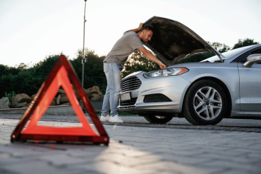 Güneş ışığı altında, kırmızı tabela, kaza, bozuk otomobil, tamir. Adam dışarıda arabasıyla bekliyor..