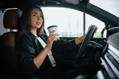 Elinde beyaz bir bardak taze içki. Güzel iş kadını yeni arabasında..