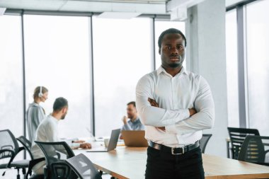 Afro-Amerikalı adam ayakta duruyor. Ofis çalışanlarından oluşan ekip içeride bir arada..