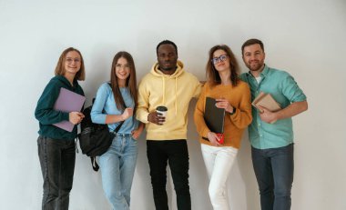 Not defterleri ve kahve fincanı tutuyor. Bir grup genç beyaz arka planda duruyor..