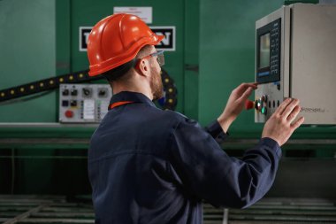 Yeşil renkli makine, operatör meşgul. Fabrika işçisi kasketli bir şekilde içeride..