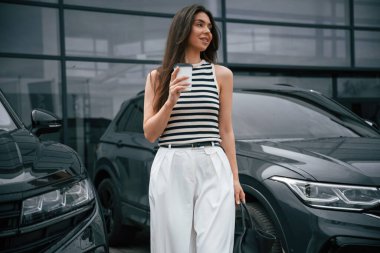 Beyaz bir kadeh ile. Çekici genç bayan dışarıda, yepyeni arabasının yanında..