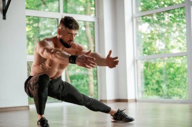 Gündüz vakti, pencerenin dışındaki ağaçlar. Güçlü kaslı adam spor salonunda çalışıyor..