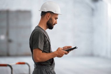 Dijital tablet kullanarak yan görünüm. Erkek işçi boş depoda..