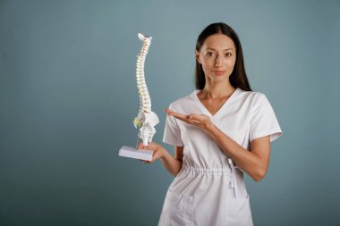 Hemşire omurga modelini elinde tutuyor. Genç kadın stüdyoda arka planda..
