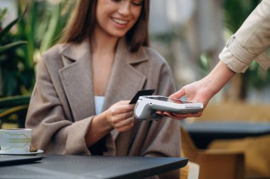 Olumlu, neşeli yüz ifadesi. Kafede yemek parasını kredi kartıyla ödeyen kadın. Kablosuz para transferi kavramı.