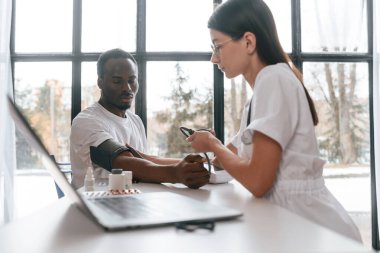 Masanın başında oturuyor. Kadın doktor bir erkeğin kan basıncını ölçer..
