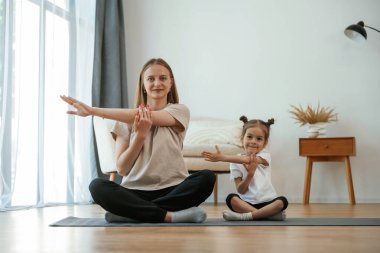 Küçük kızı olan genç bir kadın evde yoga yapıyor..