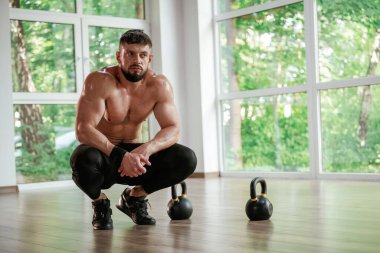 Mola verdim. Dambıllar yere. Güçlü kaslı adam spor salonunda çalışıyor..