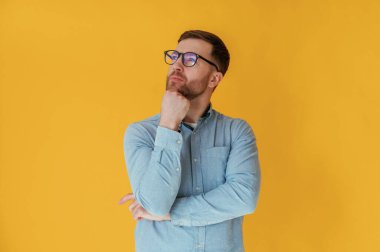 Düşünceli bir bakış, düşünme. Mavi gömlekli çekici adam sarı arka plana karşıdır..