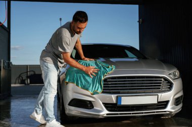 Turkuaz kumaş, aracı cilalama. Adam dışarıda arabasıyla bekliyor..