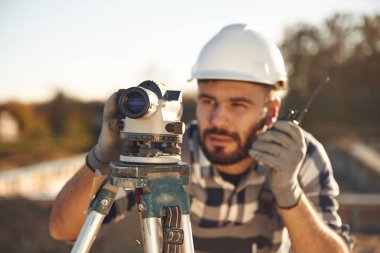 Radyoda, jeodezik optik seviyede. İşçi gündüz vakti şantiyede..