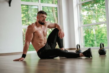 Mola verdim. Dambıllar yere. Güçlü kaslı adam spor salonunda çalışıyor..