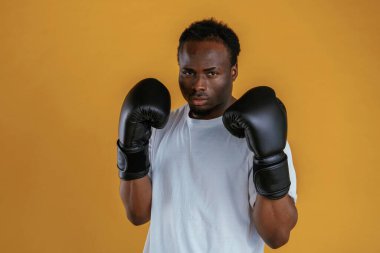 Güç kavramı. Boks eldivenleriyle. Siyah adam sarı arka plana karşı..