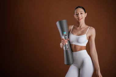 Mat ve bir şişe su ellerinde. Güzel fitness kadını stüdyoda..