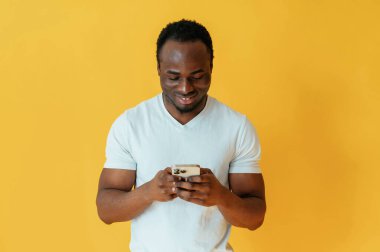 Akıllı telefonu tutmak ve gülümsemek. Siyah adam sarı arka planda stüdyoda..