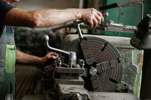 Side view. Close-up of worker's hands operating industrial machinery in workshop.