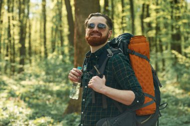 Bir şişe su, tutuyor. Sakallı adam gündüz vakti ormandadır..