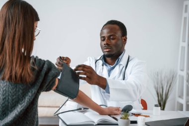 Bir doktor genç bir kadının kan basıncını ölçer..