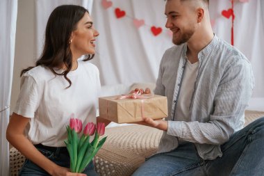 Hediye kutusu ellerinde, bayramı kutluyorlar. Genç çift evde birlikteler..