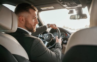 Sürücü, odaklanmış. Siyah takım elbiseli adam arabada oturuyor..