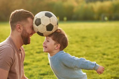Olumlu duygular, futbol topunu kafasından tutmak. Mutlu baba ve oğul yazın sahada eğleniyorlar..