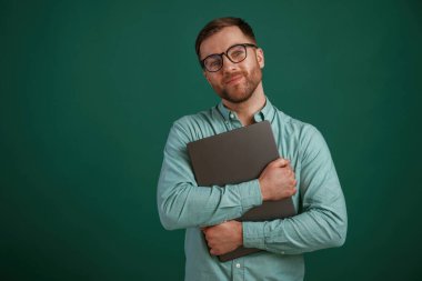 Gümüş renkli dizüstü bilgisayar ellerinde. Adam stüdyoda arka planda duruyor..