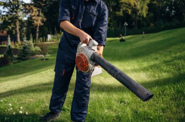 Yaprak üfleyiciyle çalışıyor. Bahçede profesyonel bahçıvan var..