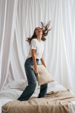 Yastıkla zıplıyor. Genç ve güzel bir kadın evde, yatağın üzerinde..