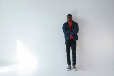 Kollarını kavuşturarak poz vermek. Stüdyoda beyaz arka plana karşı siyah adam var..