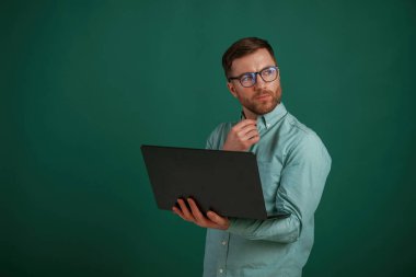 Gümüş renkli dizüstü bilgisayar ellerinde. Adam stüdyoda arka planda duruyor..