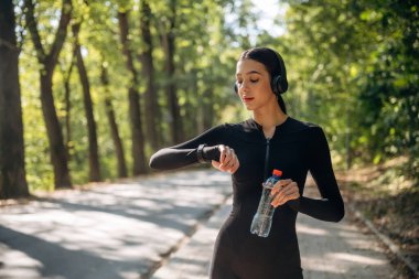 Saate, saate, izleyiciye bakıyorum. Genç, sıska kadın dışarıda siyah spor kıyafetleri giyiyor..
