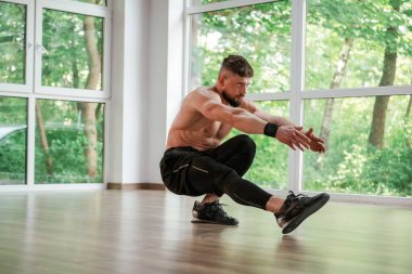 Gündüz vakti, pencerenin dışındaki ağaçlar. Güçlü kaslı adam spor salonunda çalışıyor..