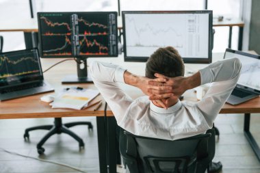 Ellerin başının arkasında oturuyorsun. İşadamı bilgisayar başında ve ofiste çalışıyor..