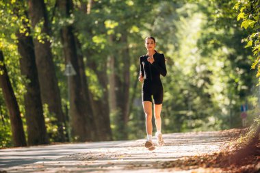 Koşu, ön manzara. Genç, sıska kadın dışarıda siyah spor kıyafetleri giyiyor..