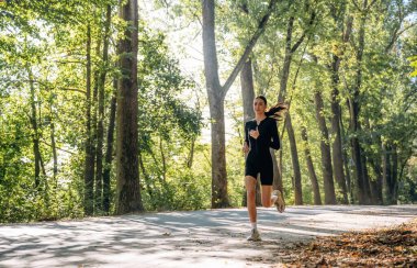 Koşmak, ormanda koşmak. Genç, sıska kadın dışarıda siyah spor kıyafetleri giyiyor..