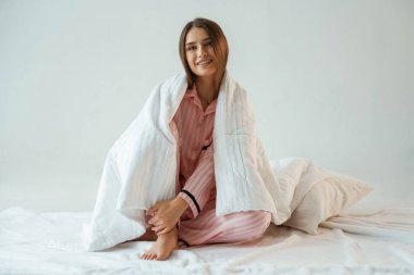 Rahatlıyorum, beyaz battaniyeyle oturuyorum. Genç ve güzel bir bayan stüdyoda arka plana karşı..