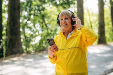 Akıllı telefon ellerde. Sarı spor ceketli son sınıf öğrencisi kulaklıklarla dışarıda bekliyor..
