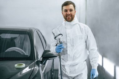 Parlak yapay ışıklandırma. Adam ayakta duruyor ve elinde otomobil boyasıyla sprey tabanca tutuyor..