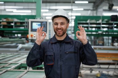 Makineye karşı. Fabrika işçisi kasketli bir şekilde içeride..